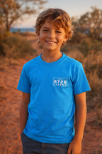 Smiling boy wearing the 6725 Logo Kids Tee in ocean-blue, showcasing Broome style on a sunny day.