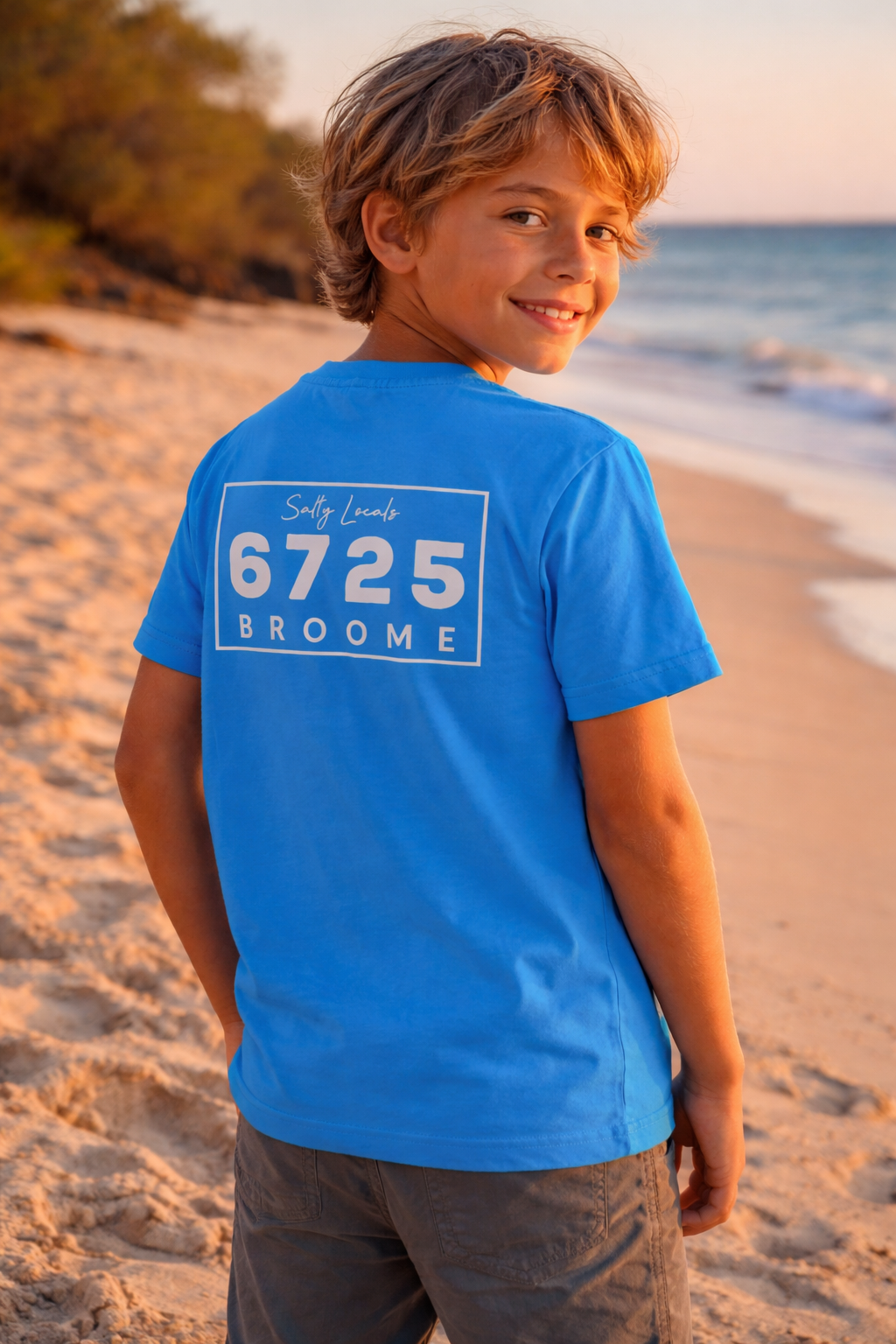 Child wearing 6725 Logo Kids Tee on the beach at sunset in Broome, showcasing the iconic ocean-blue design.