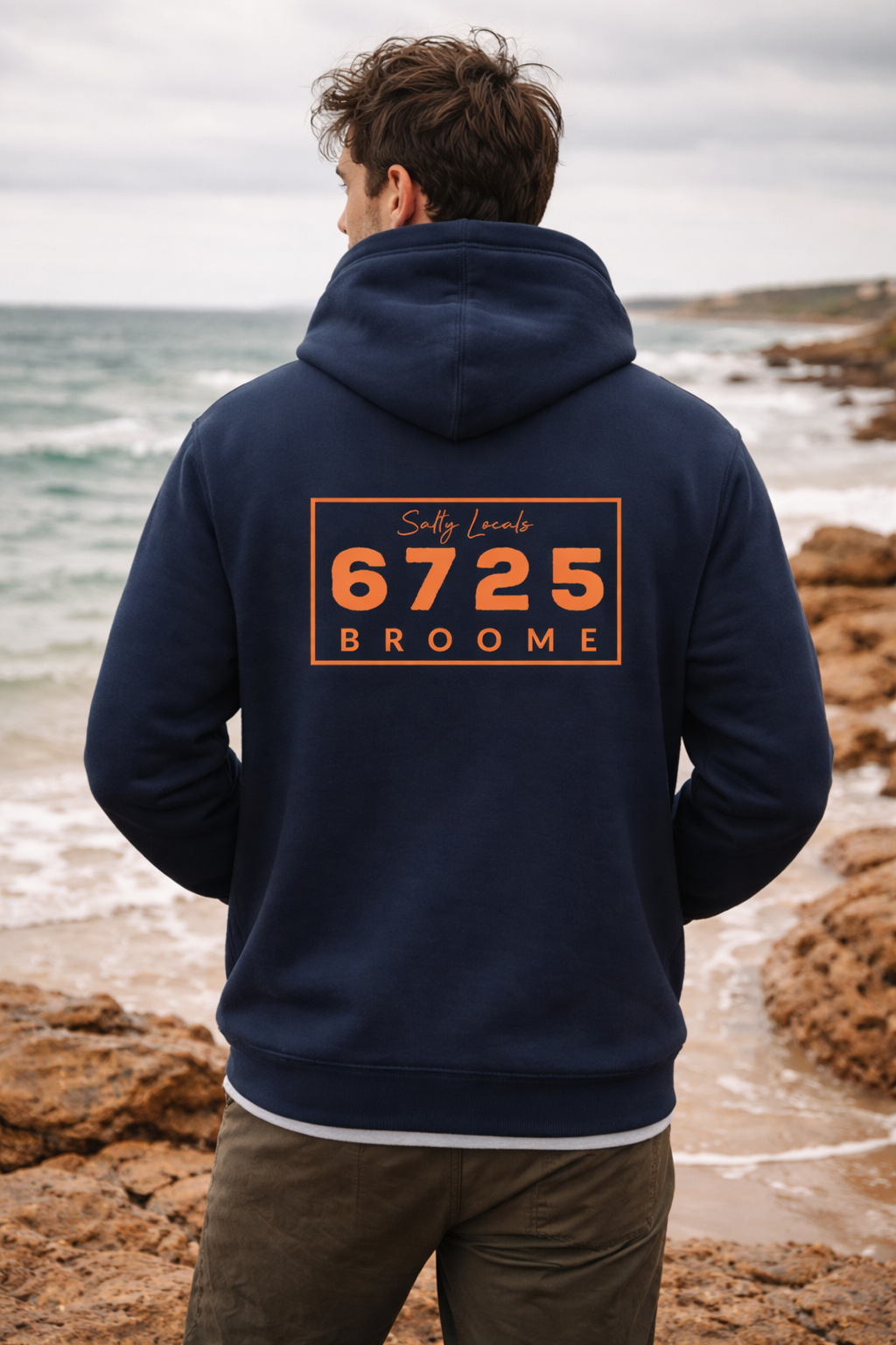 6725 Zip Up Men's Hooded Jacket worn by a man standing on a rocky beach with a navy color and bold chest print.
