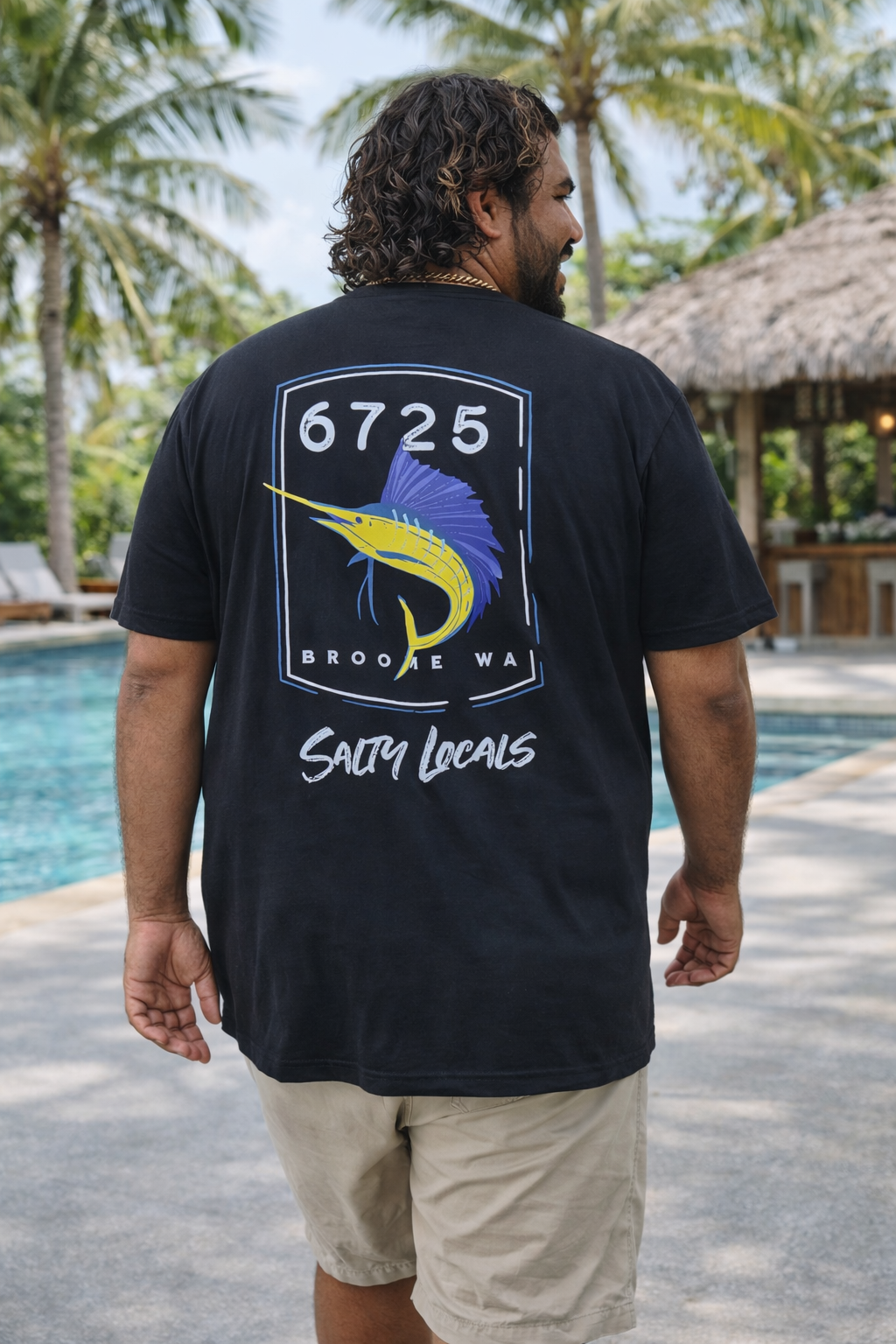 Back view of a man wearing the 6725 Sword Adult Tee by the pool, showcasing its coastal style and relaxed fit.