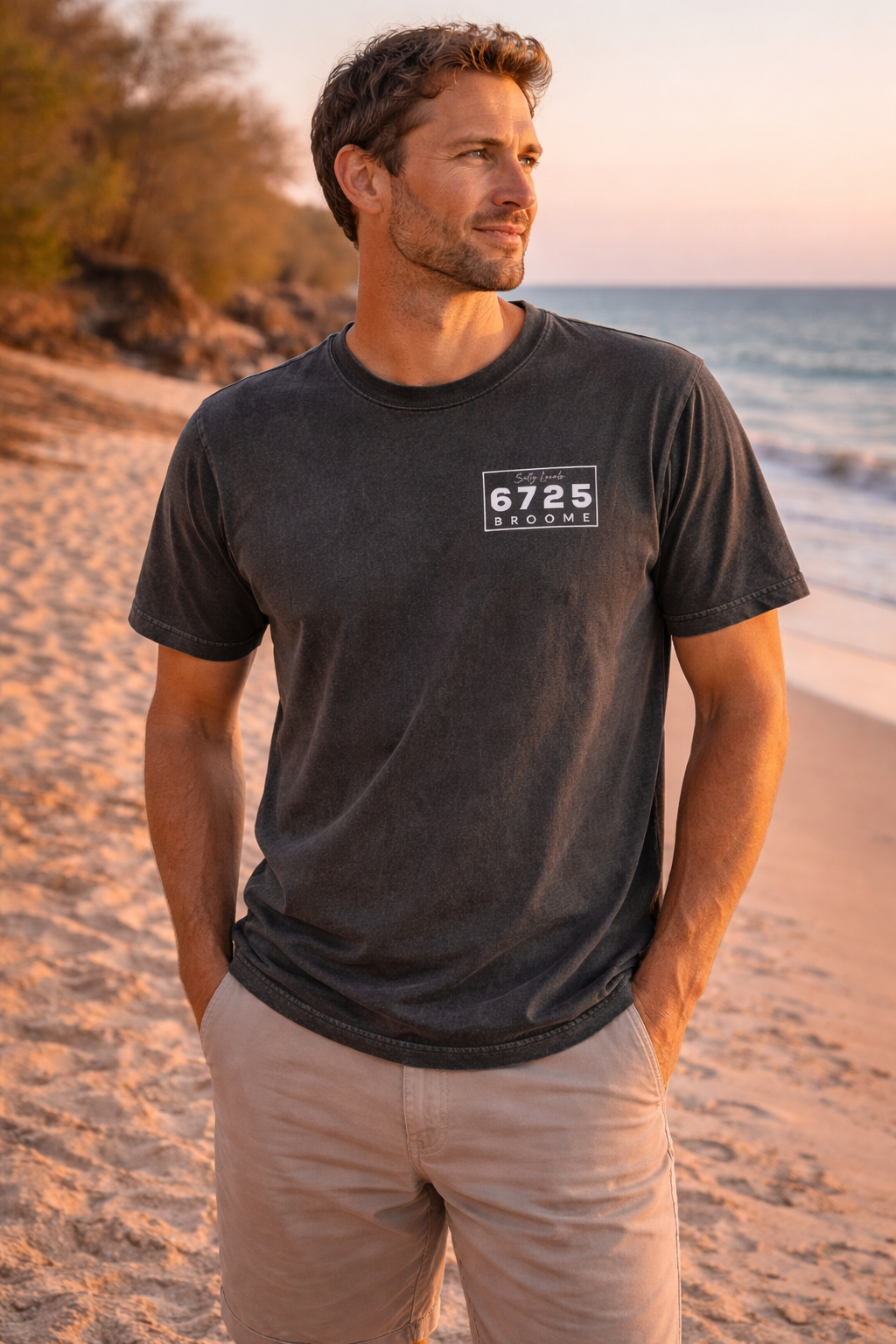 Men's Stonewash T-Shirt - Black model standing on beach at sunset, showcasing 6725 Broome branding.
